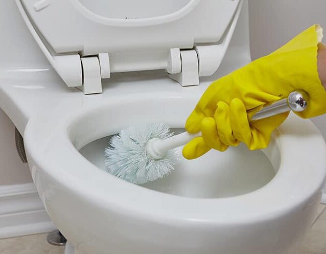 Frau reinigt Toilette mit Handschuhen und Toilettenbürste